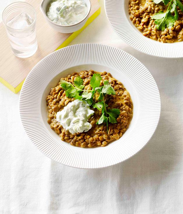 A clean white bowl of Coconut Lentil Dhal with cucumber yoghurt and parsley leaves on top
