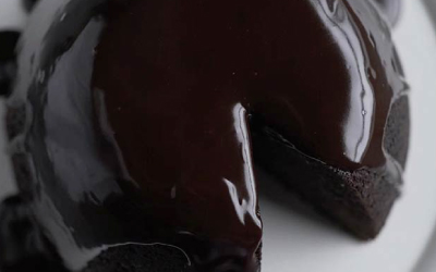 Glossy dark Chocolate Christmas Pudding on a white serving plate with a slice missing