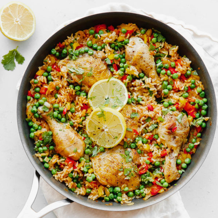 A frying pan containing Arroz Con Pollo and chicken with lemon slices on top