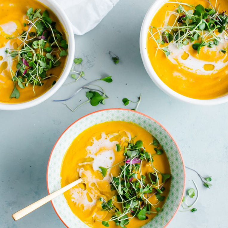 Three bowls of Garam Marsala Carrot soup with coconut milk and green sprouts sprinkled on top