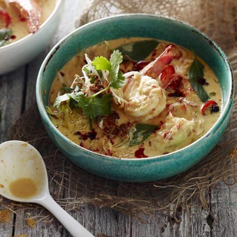 A blue bowl of Prawn Laksa and white serving spoon
