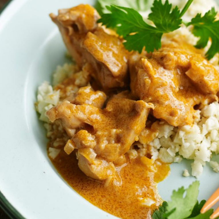 A white plate with Paleo Butter Chicken and parley leaves on top